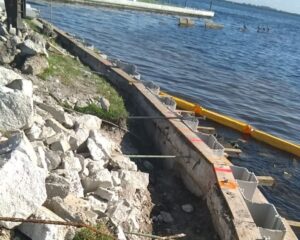 A concrete retaining seawall under repair next to a body of water.