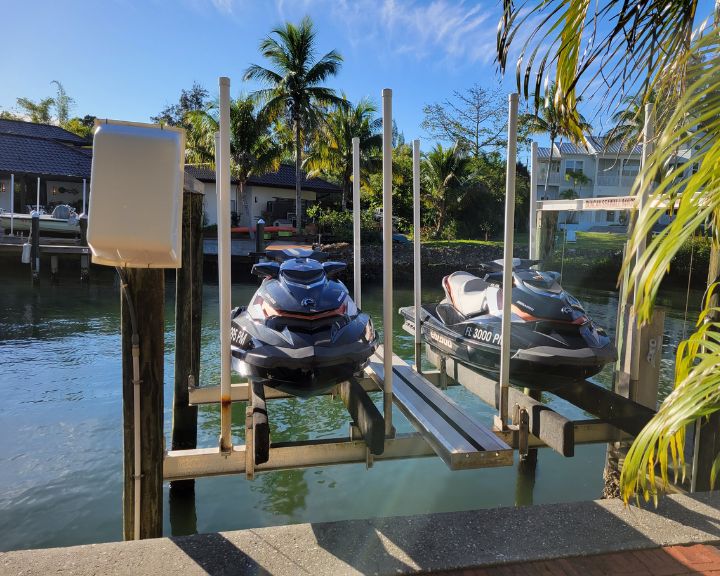Two jet skis are parked on a boat lift next to palm trees.