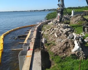 A construction crew is working on a retaining seawall near a body of water.